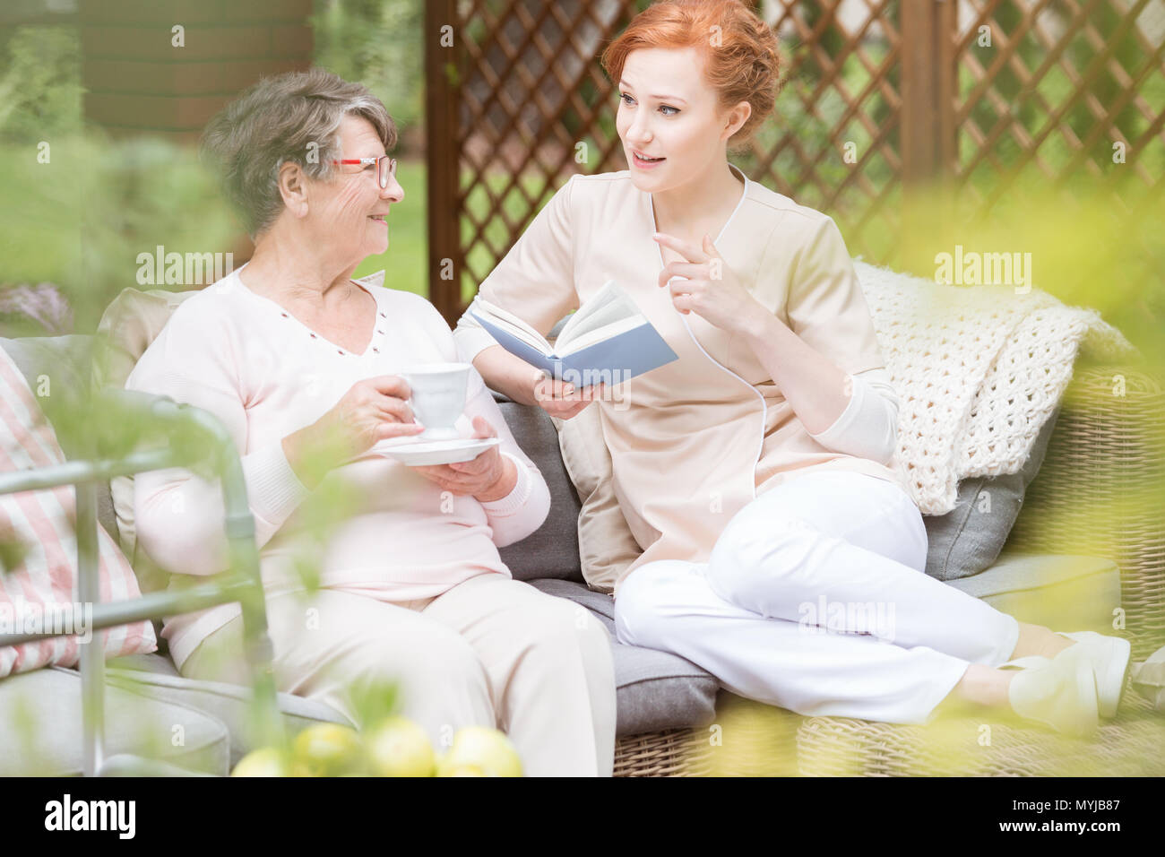 Lectura del cuidador de un libro para una mujer mayor de beber té en la terraza Foto de stock