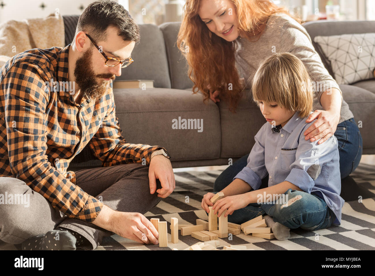 Los padres jóvenes jugando con su hijo con bloques de madera en la espaciosa sala de estar Foto de stock