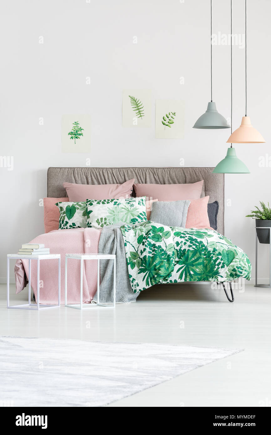 Camas florales verdes en la cama tamaño king en el dormitorio con lámparas y carteles en la pared Foto de stock