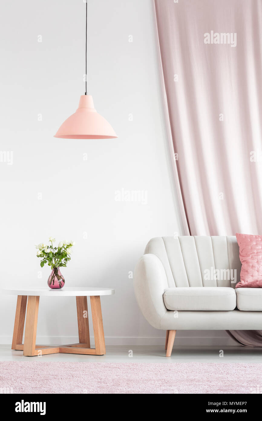 Luminoso salón interior con sofá de color beige, melocotón, lámpara, mesa de madera y rosas en jarrón rosa Foto de stock