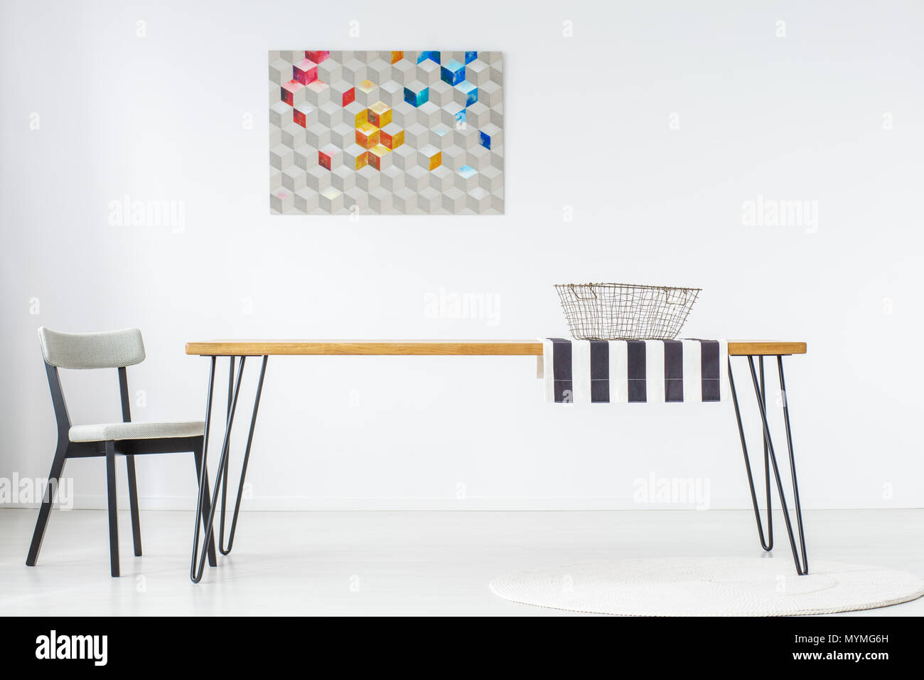 Cartel en la pared blanca y gris silla de comedor con canasta metálica sobre tela a rayas, sobre mesa de madera Foto de stock