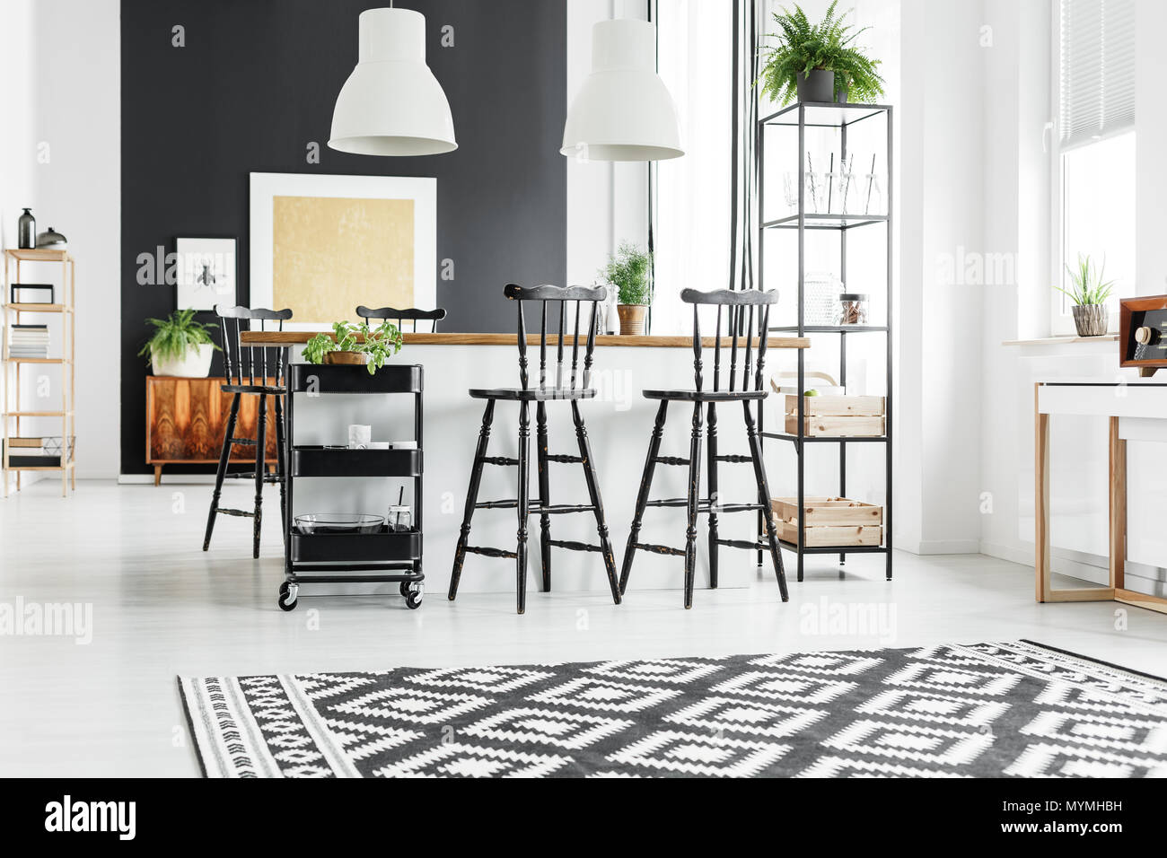 Alfombras geométricas en blanco y negro en la rústica cocina con taburetes en la encimera de madera Foto de stock
