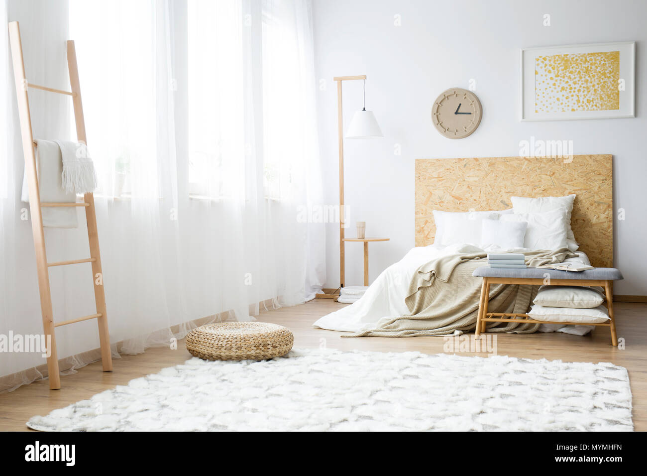Reloj moderno colgando sobre una cama doble con almohadas rellenas de una blanca interior del dormitorio Foto de stock