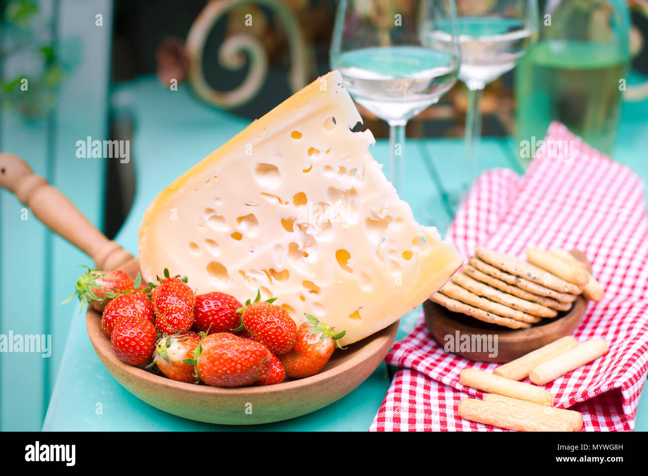 Queso holandés con agujeros y fresa. En un vaso de vino blanco y