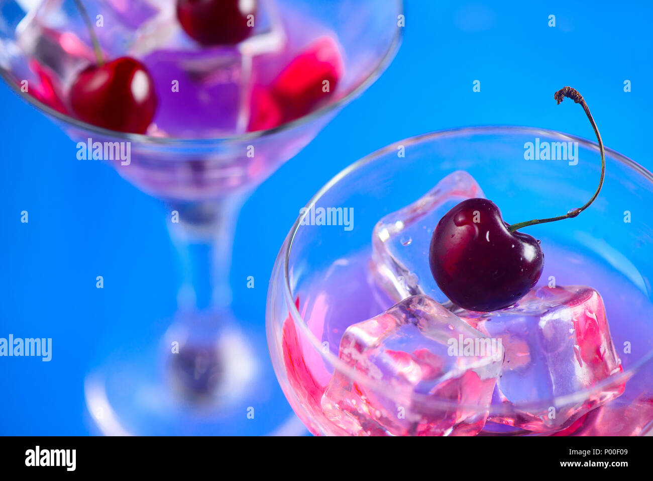 Cóctel de cerezas cerca. Copa de Martini con cubitos de hielo y las cerezas en un fondo azul brillante con espacio de copia. Día de verano refrescante concepto Foto de stock