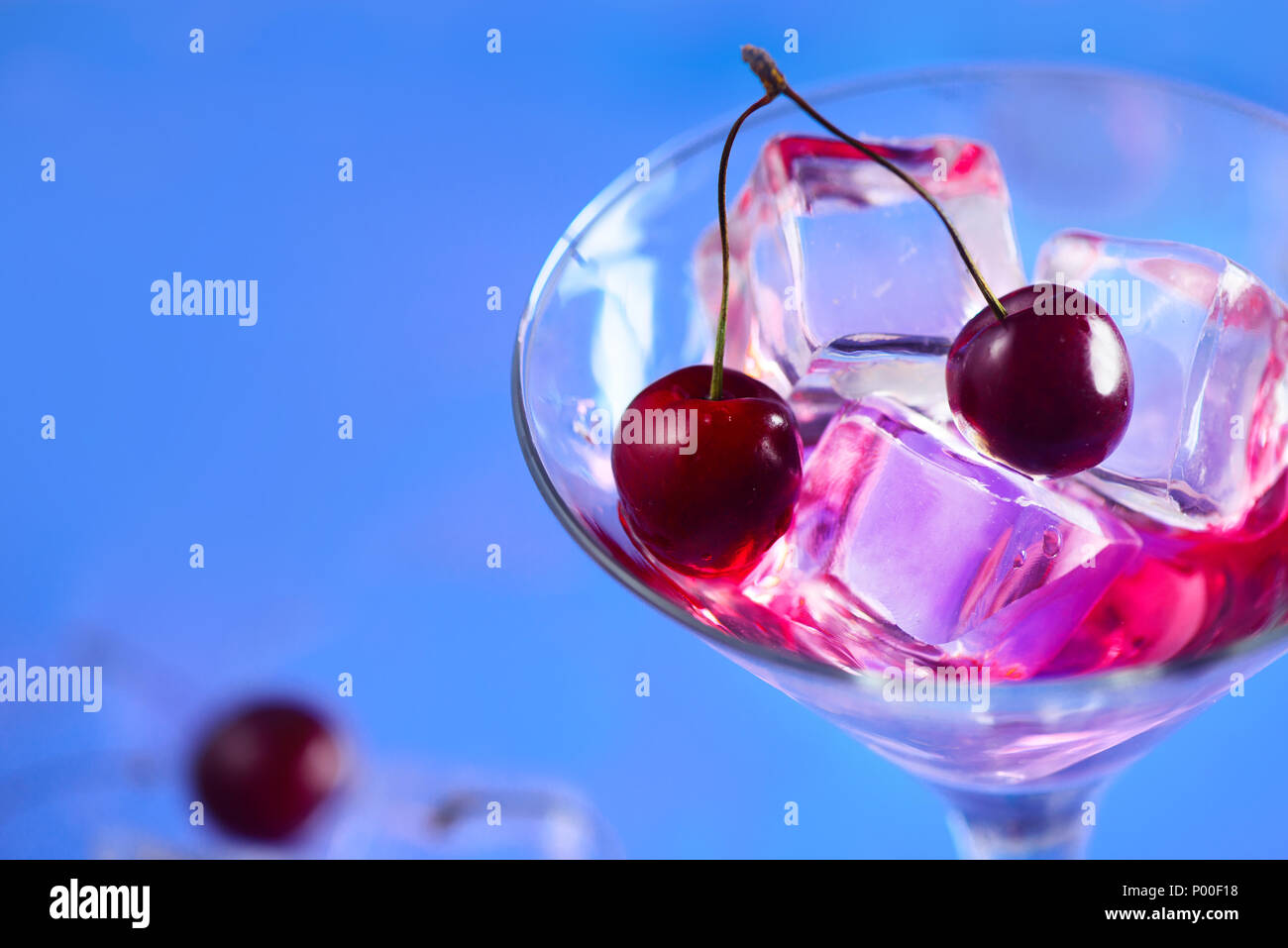 Cóctel de cerezas cerca. Copa de Martini con cubitos de hielo y las cerezas en un fondo azul brillante con espacio de copia. Día de verano refrescante concepto Foto de stock