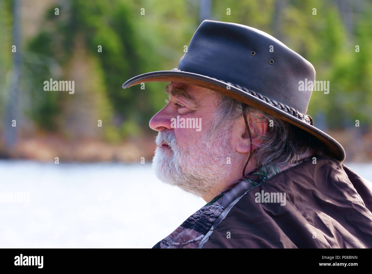 Cerca de un pacífico hombre caucásico, 50's, llevaba una larga barba  blanca, un sombrero de cuero estilo australiano y un abrigo de camuflaje,  es la pesca en su barca en un l
