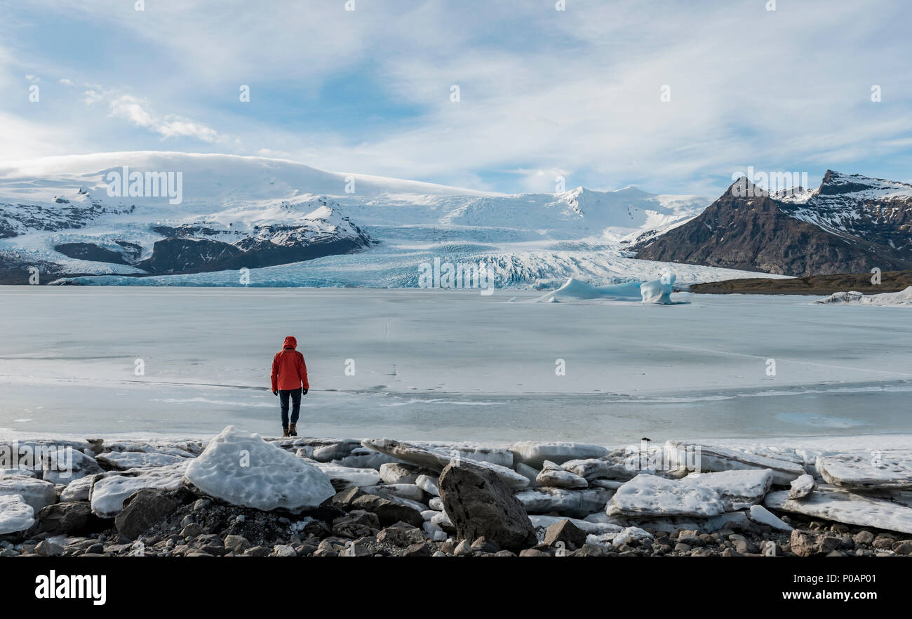 El hombre permanece congelada en la laguna con témpanos, montañas, laguna glaciar Fjallsárlón, al sur de Islandia, Islandia Foto de stock