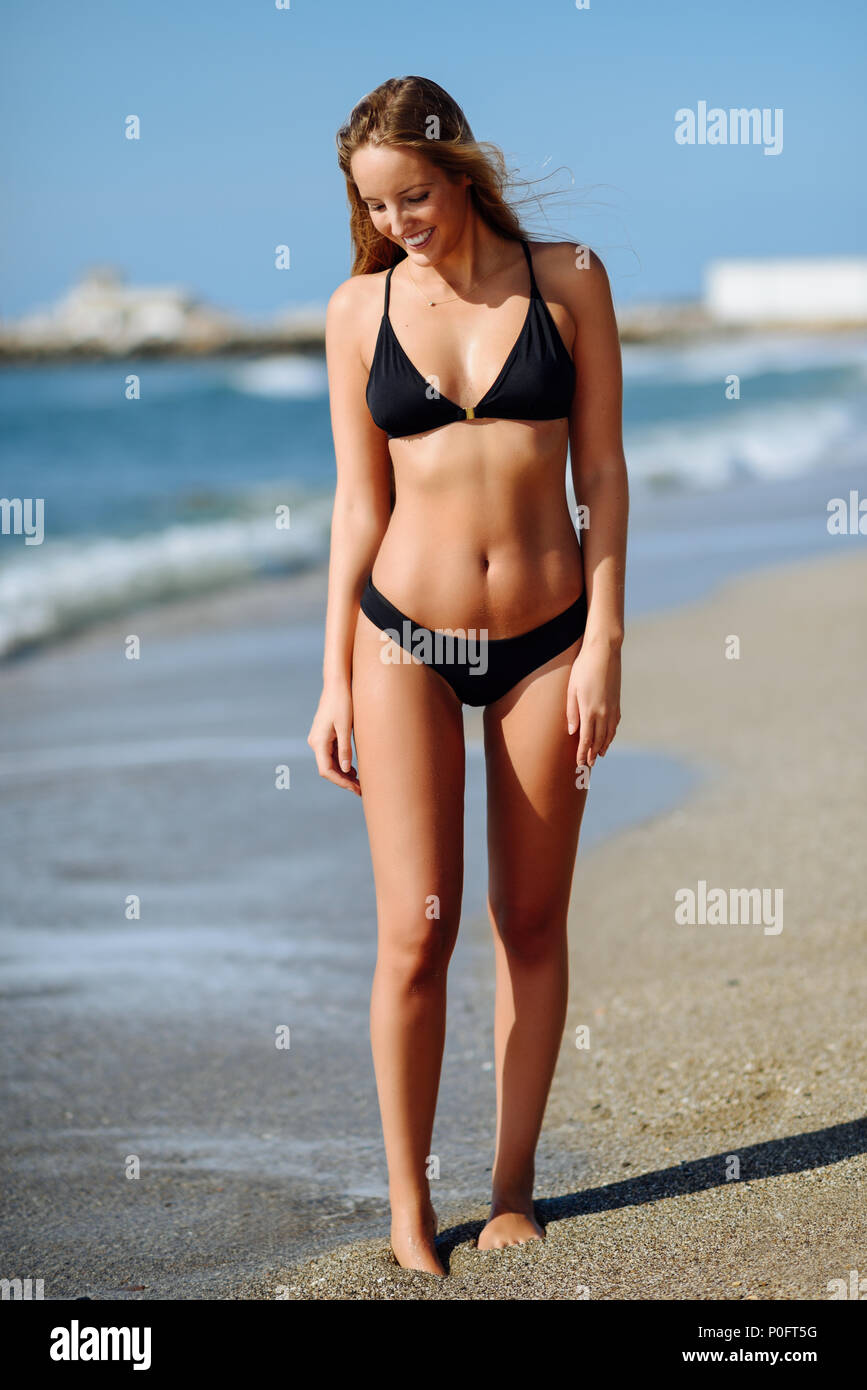Joven Mujer rubia con hermoso cuerpo en traje de baño caminando en una  playa tropical. Mujeres caucásicas con recto largo peinado vistiendo negro  bikini smi Fotografía de stock - Alamy