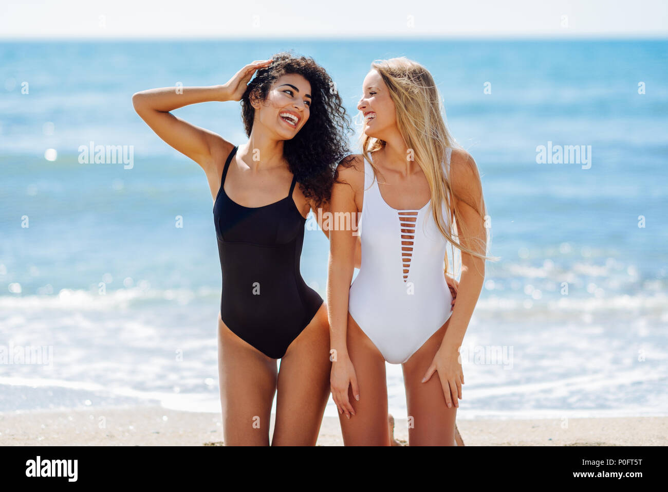 jóvenes en traje de en una playa tropical. Gracioso caucásica árabe mujeres vistiendo trajes de baño blanco y negro arrodillado en la playa Fotografía de stock - Alamy