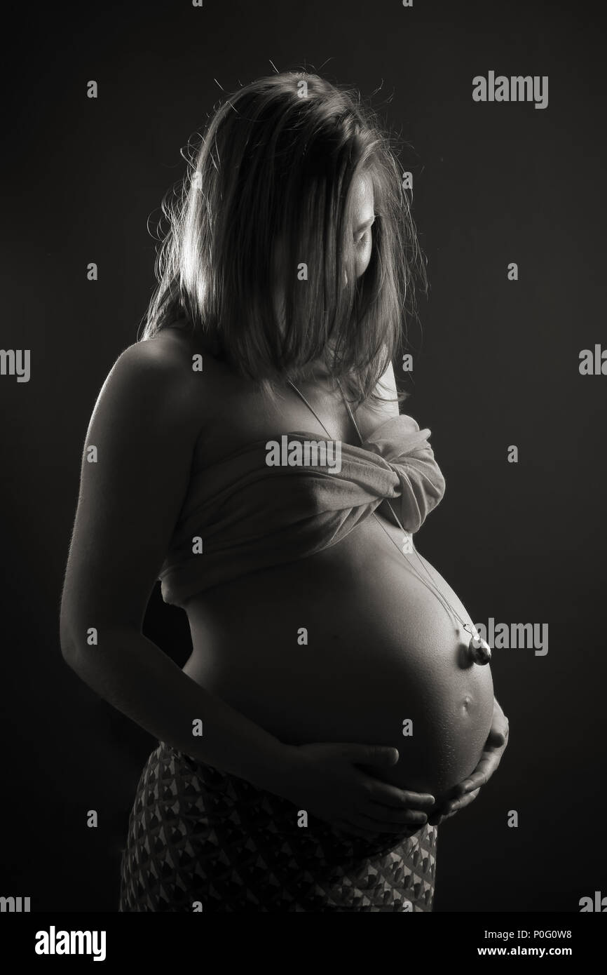 Retrato de estudio de la mujer embarazada vestidos de campana, tocando el vientre, blanco y negro Foto de stock