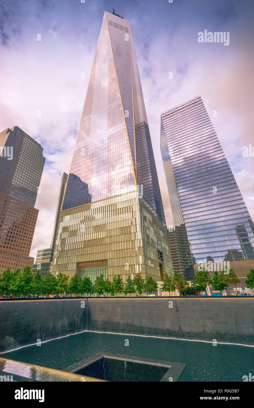 En el primer plano el monumento a las víctimas de la tragedia de 9/11 y en el fondo el nuevo World Trade Center se eleva de manera desafiante Foto de stock