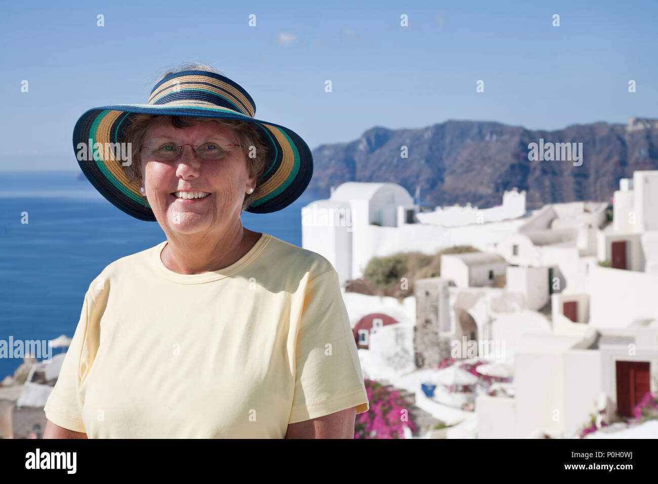 Senior Citizen sonriendo por el océano, teniendo un gran momento mientras viaja con la famosa arquitectura griega Foto de stock
