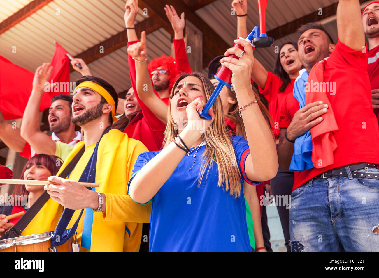 Grupo de aficionados vestidos de diversos colores viendo un evento deportivo en las gradas de un estadio Foto de stock