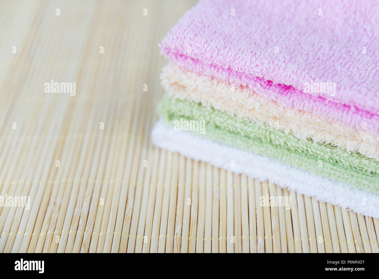 Pila de terry toallas limpias multicolor sobre una estera de bambú, con espacio para texto Foto de stock