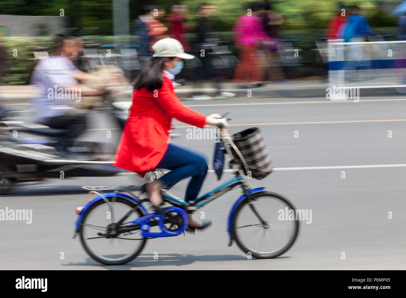 Yangzhou, Jiangsu, China. Mujer con máscara respiratoria en bicicleta. Foto de stock