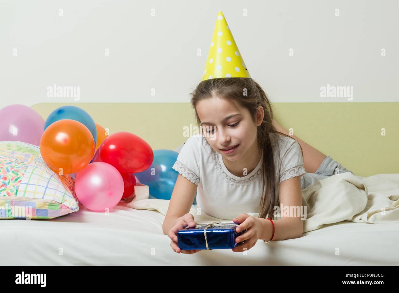El cumpleaños de una adolescente es de 10-11 años. Una Niña de sombrero,  una fiesta con un regalo en la cama en una habitación infantil, globos de  fondo Fotografía de stock - Alamy