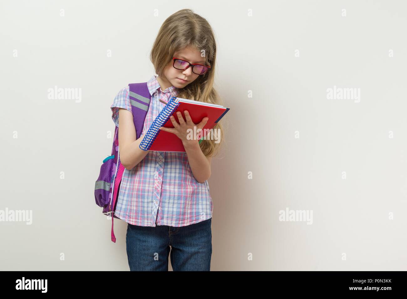 Niña estudiante de primaria con gafas con una mochila escrito en su cuaderno.  Escuela brillante pared de fondo Fotografía de stock - Alamy