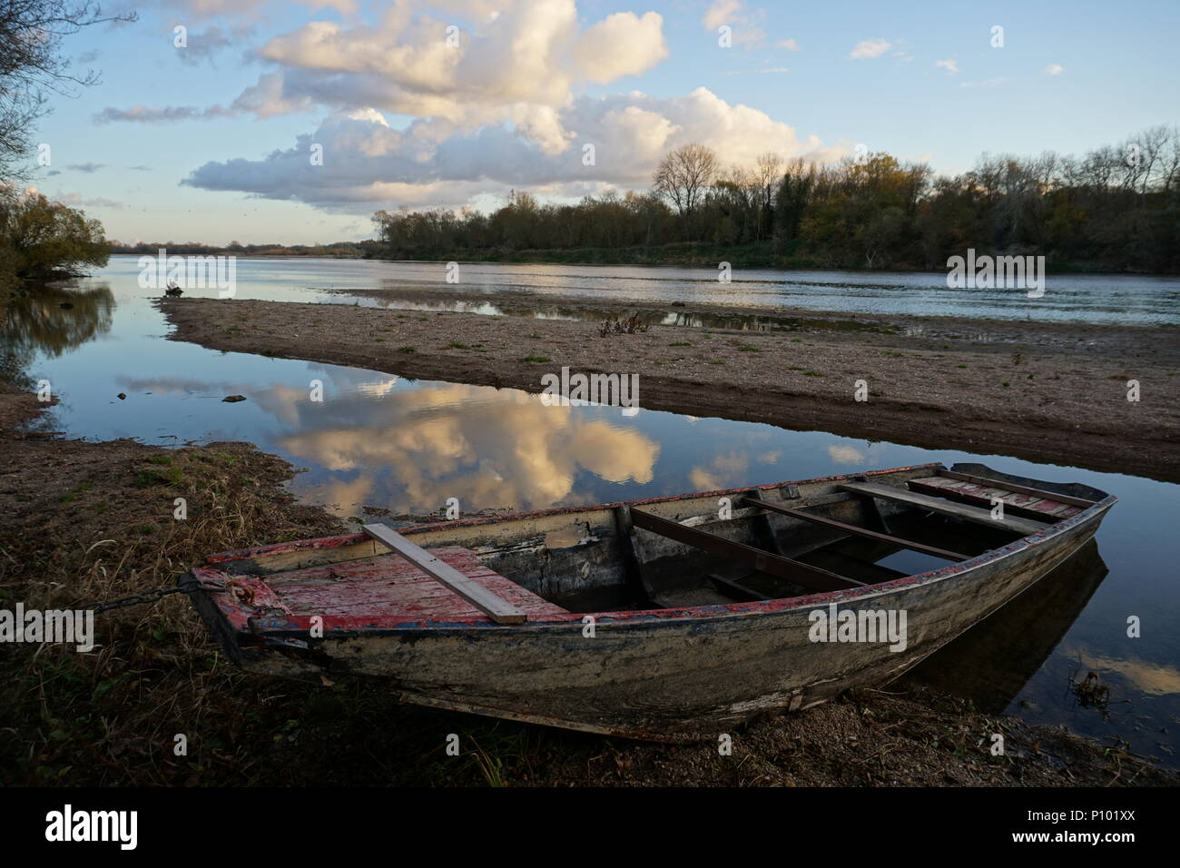 Reflejo de espejo en el río Loira, Francia de un claro atardecer con nubes hinchadas de madera antigua y un típico barco anclado en la playa Foto de stock