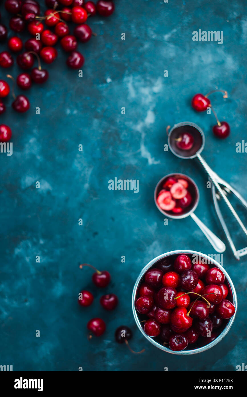 Cerezas con una cuchara de helado y la cuchara de metal sobre un fondo de cemento gris, Verano bayas concepto con espacio de copia. Los tonos de color neutral todavía lif Foto de stock