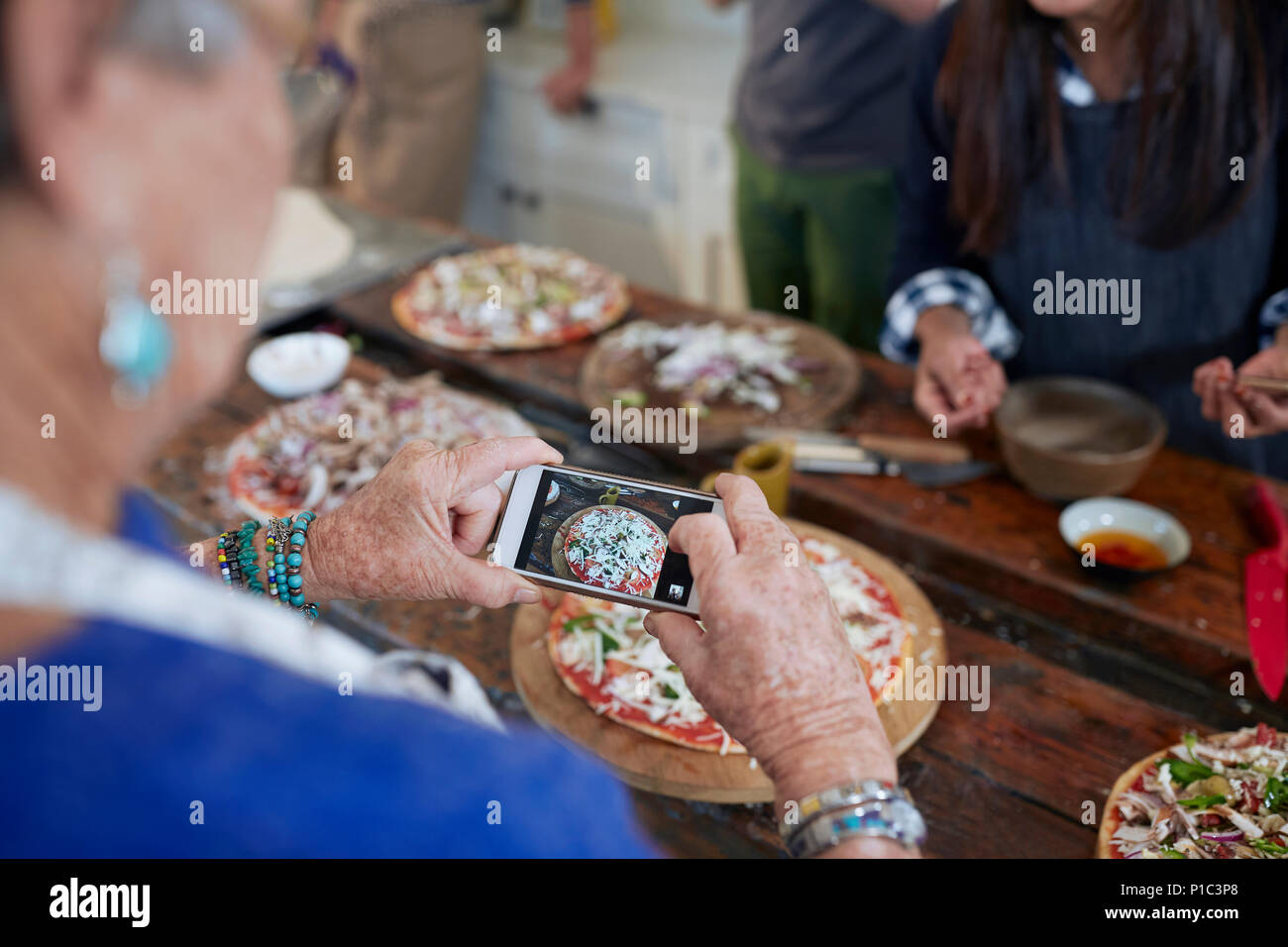 Mujer de más edad con cámara teléfono fotografiar pizza casera en clase de cocina Foto de stock