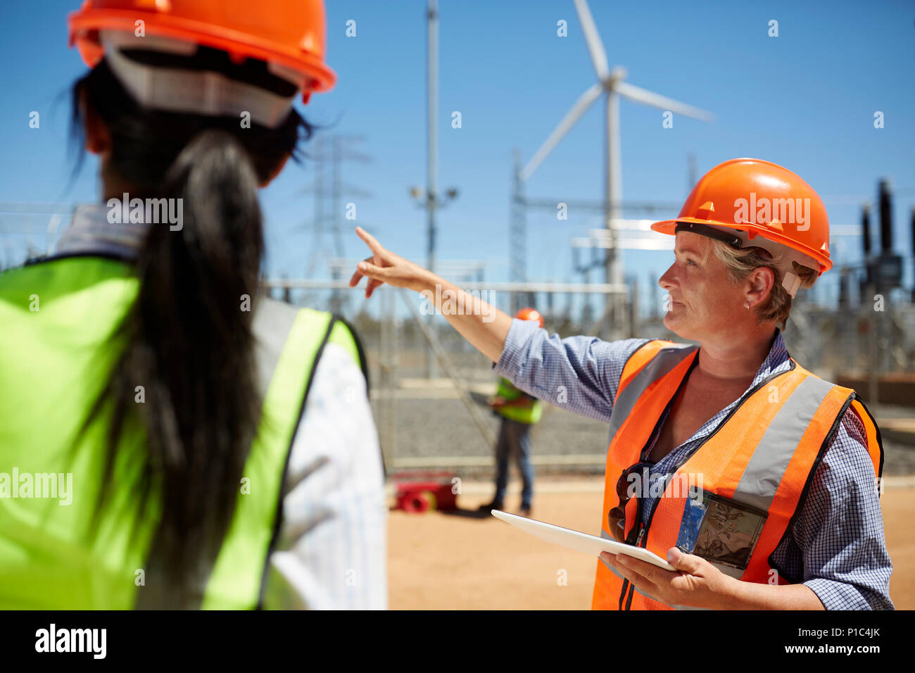 Ingeniero hembra con tableta digital hablando a un colega en la planta de energía de turbinas eólicas Foto de stock