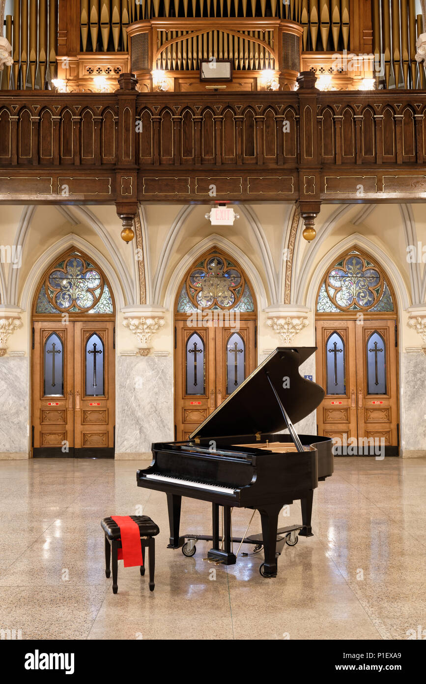 Baby Grand Piano listo para jugar con la tapa abierta en el interior de la iglesia con tres hermosas puertas de roble y ventanas de vidrio de color detrás de antigüedades, circa 1904. Foto de stock