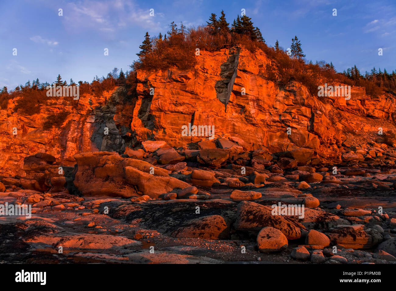 Puesta de sol ilumina la escarpada costa adyacente a la arena de la Playa Fluvial, Nova Scotia, Canadá Foto de stock