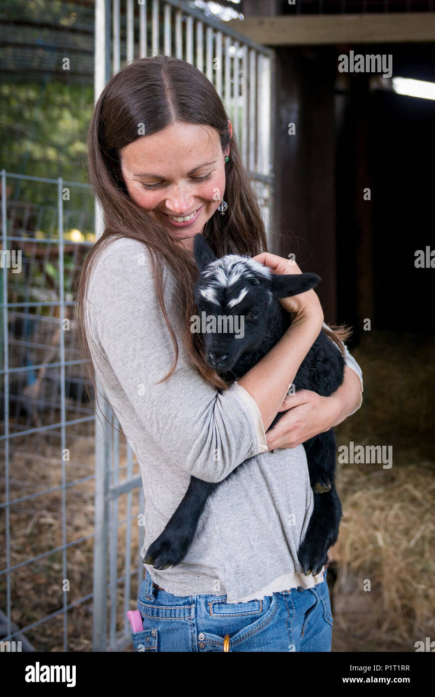 Retrato de una mujer atractiva con un bebé ovejas negras en un entorno rural. Foto de stock