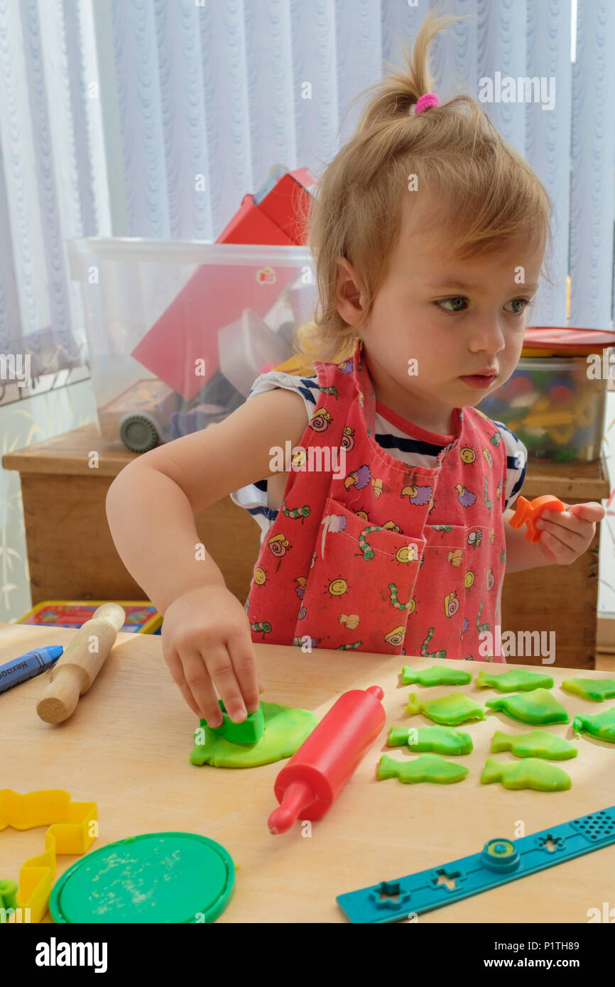 Aprender a través del juego. Feliz joven niña de dos años jugando y cortando el modelado de la masa de arcilla. Foto de stock