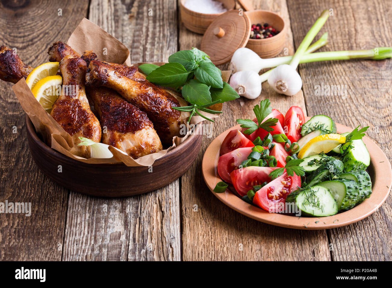 Muslos de pollo asado en cuenco de cerámica y hortalizas frescas sobre mesa de madera rústica, comida favorita Foto de stock