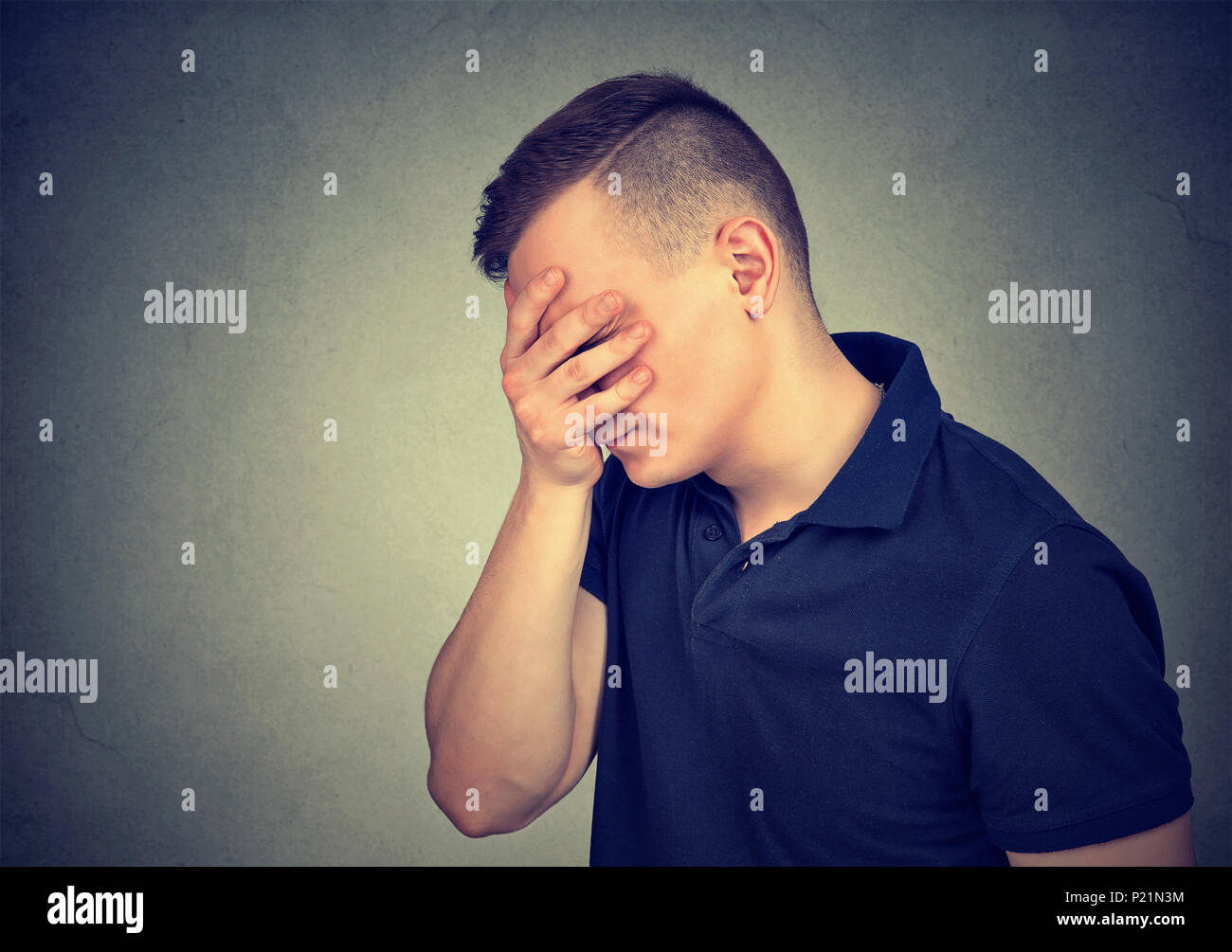 El perfil lateral de un hombre triste y con las manos sobre su rostro aislado sobre fondo gris Foto de stock