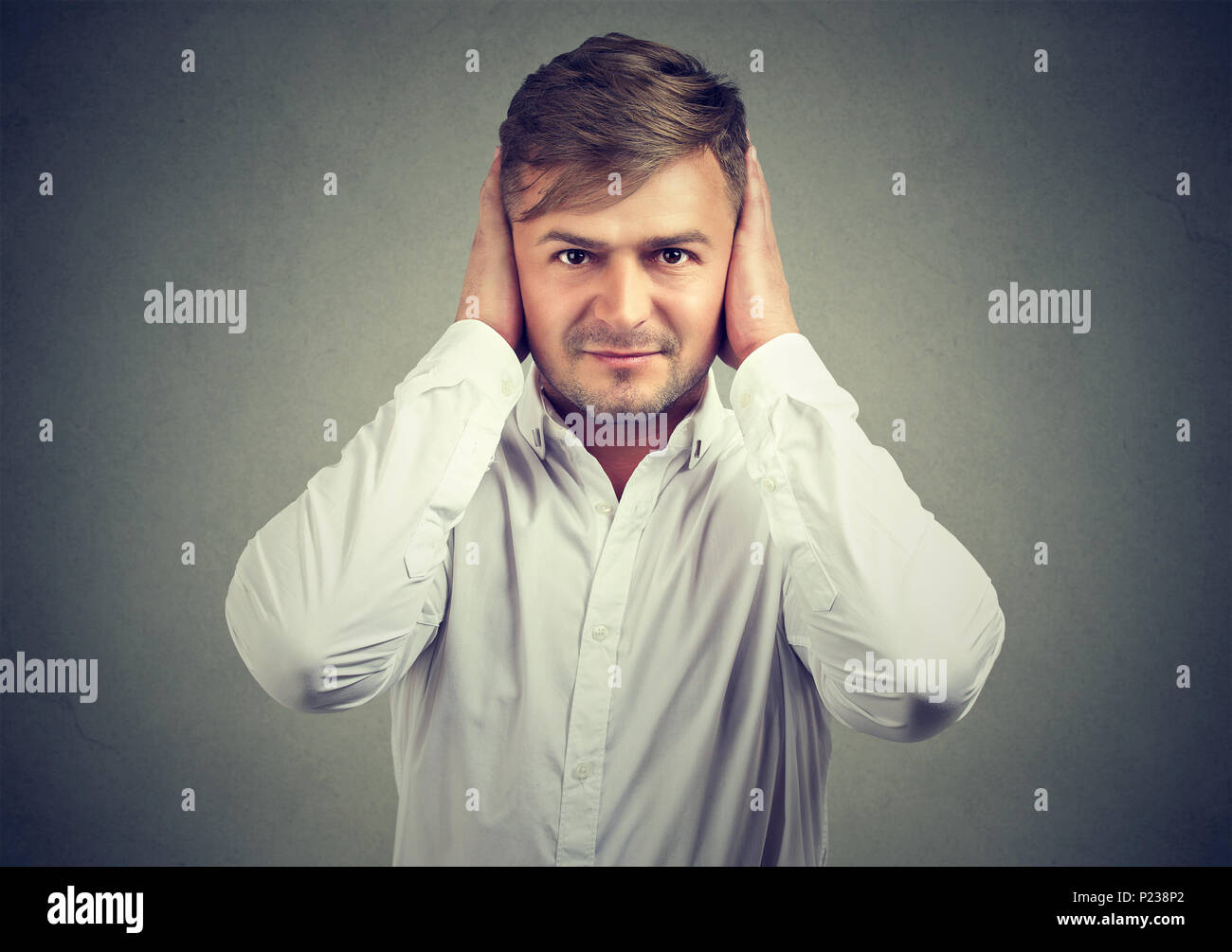 El hombre con la camisa blanca que cubre los oídos con las manos ignorando el ruido y pidiendo tranquilo. Foto de stock