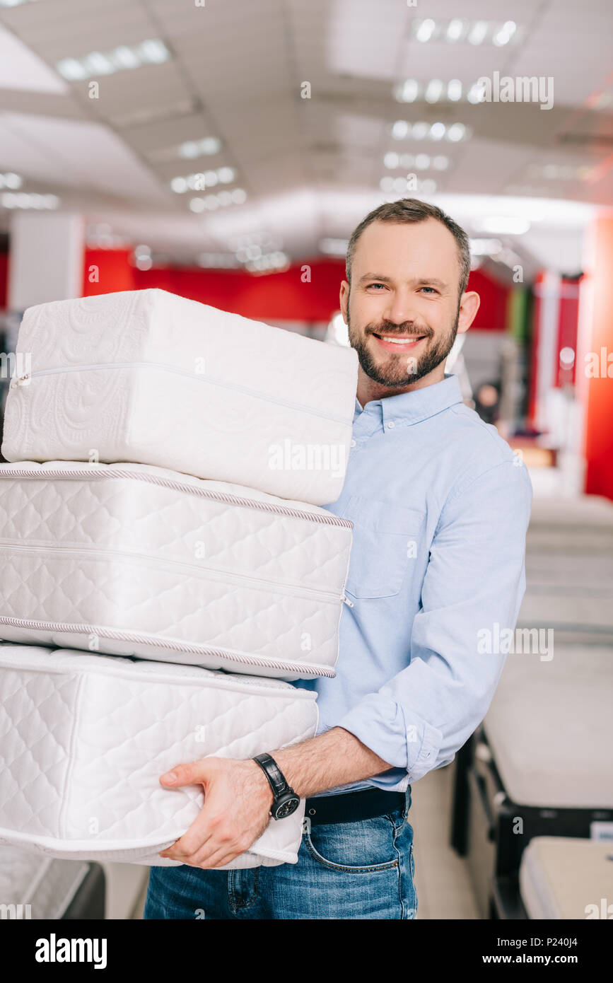 Hombre sonriente Celebración montón de colchones plegables en manos en  tienda de muebles Fotografía de stock - Alamy