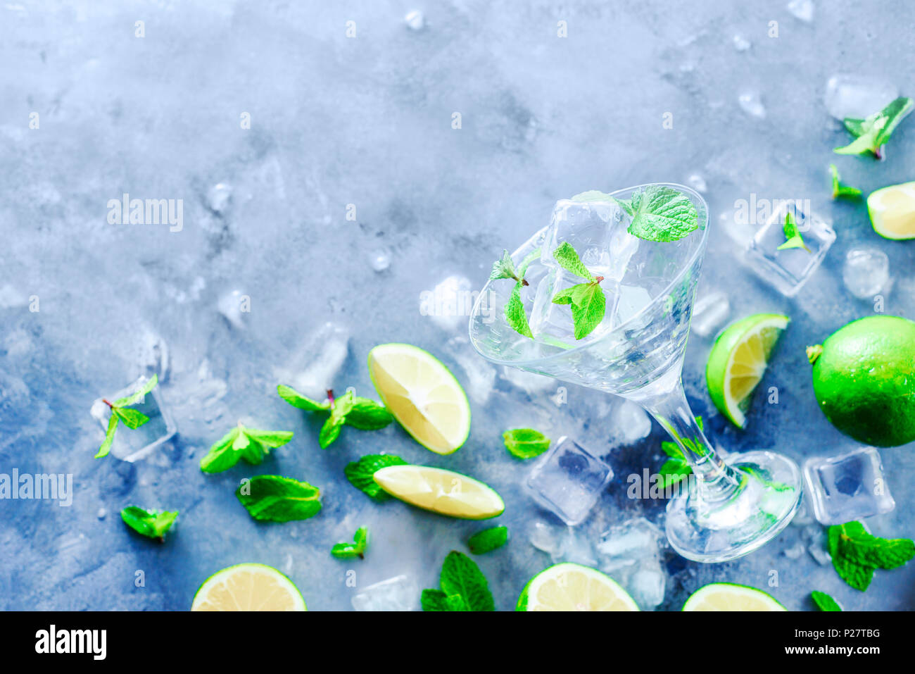 Copa de Martini con cóctel mojito ingredientes, Menta, Limón y cubitos de hielo sobre un fondo de piedra. Refresco de verano laicos plana. Preparar bebidas concepto Foto de stock