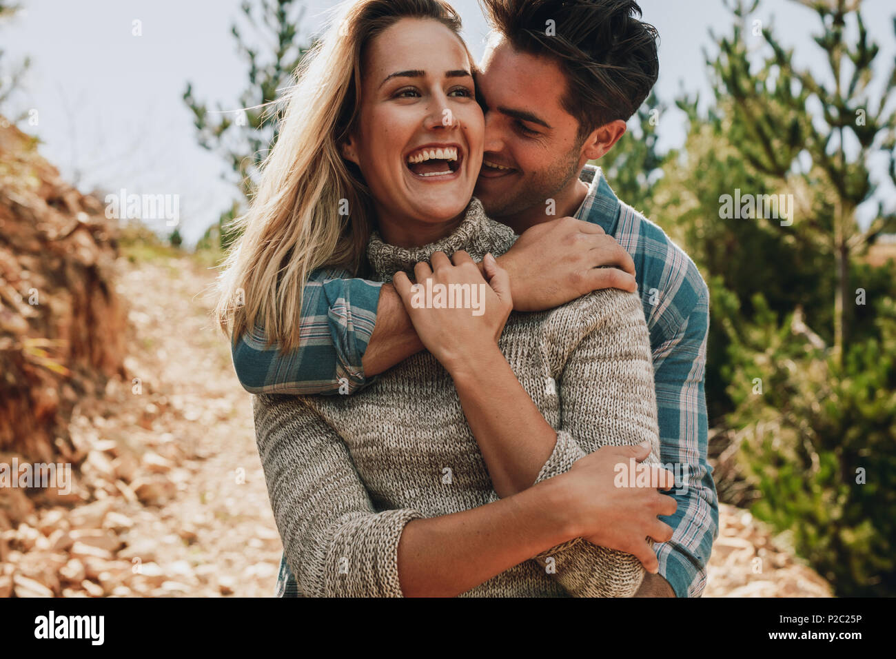 Guapo sonriente abrazando a su novia por detrás. Feliz pareja joven afuera. Foto de stock