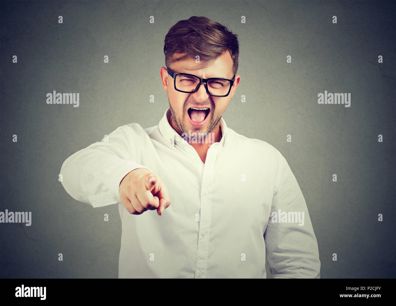 Hombre casual en las gafas y camisa blanca apuntando a la cámara y gritando de culpar y acusar a Foto de stock