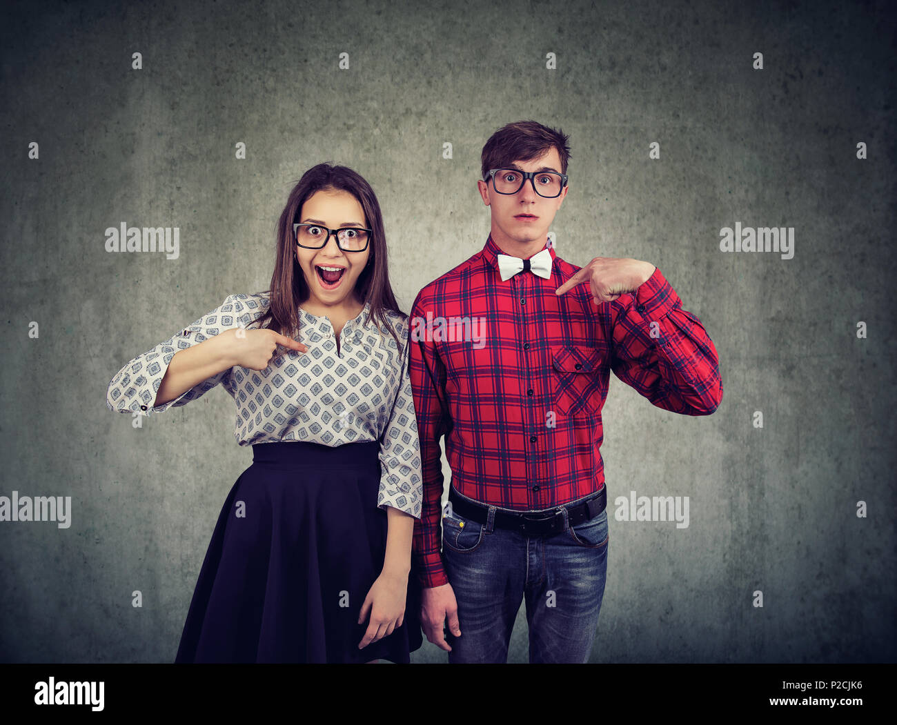 Aturdido joven hombre y mujer todos juntos y apuntando a sí mismos ser seleccionado Foto de stock