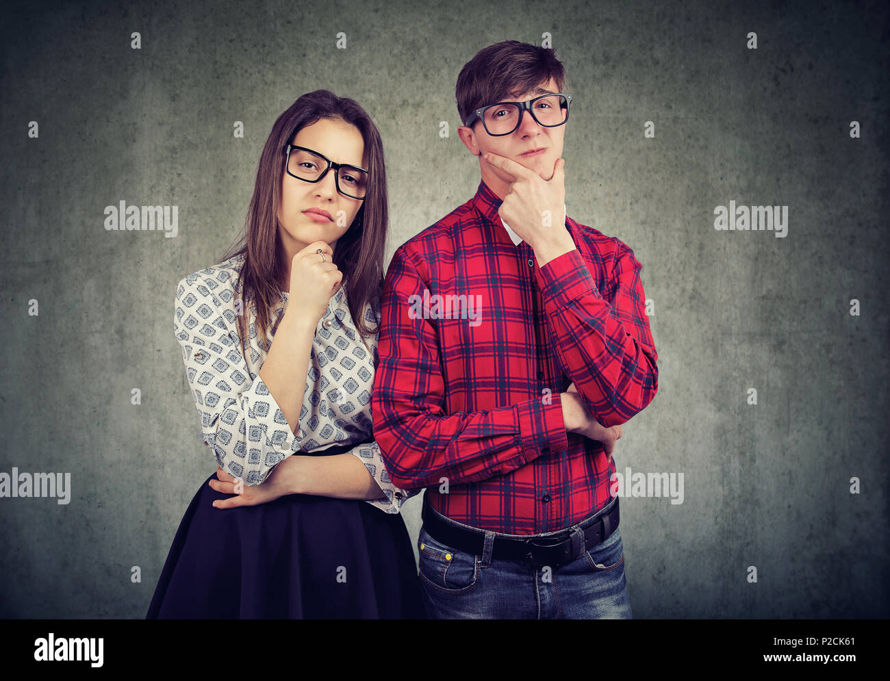 Pareja ocasional en vidrios de tocar los rostros y mirando con incredulidad y desconfianza en la cámara sobre fondo gris Foto de stock