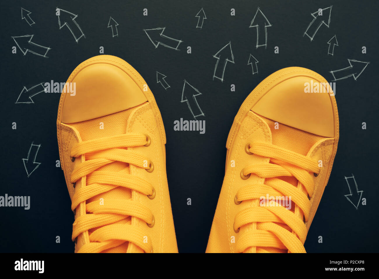 La toma de decisiones y elecciones correctas imagen conceptual con amarillo zapatillas sobre la carretera con pequeñas huellas de flecha apuntando a diferentes direcciones Foto de stock