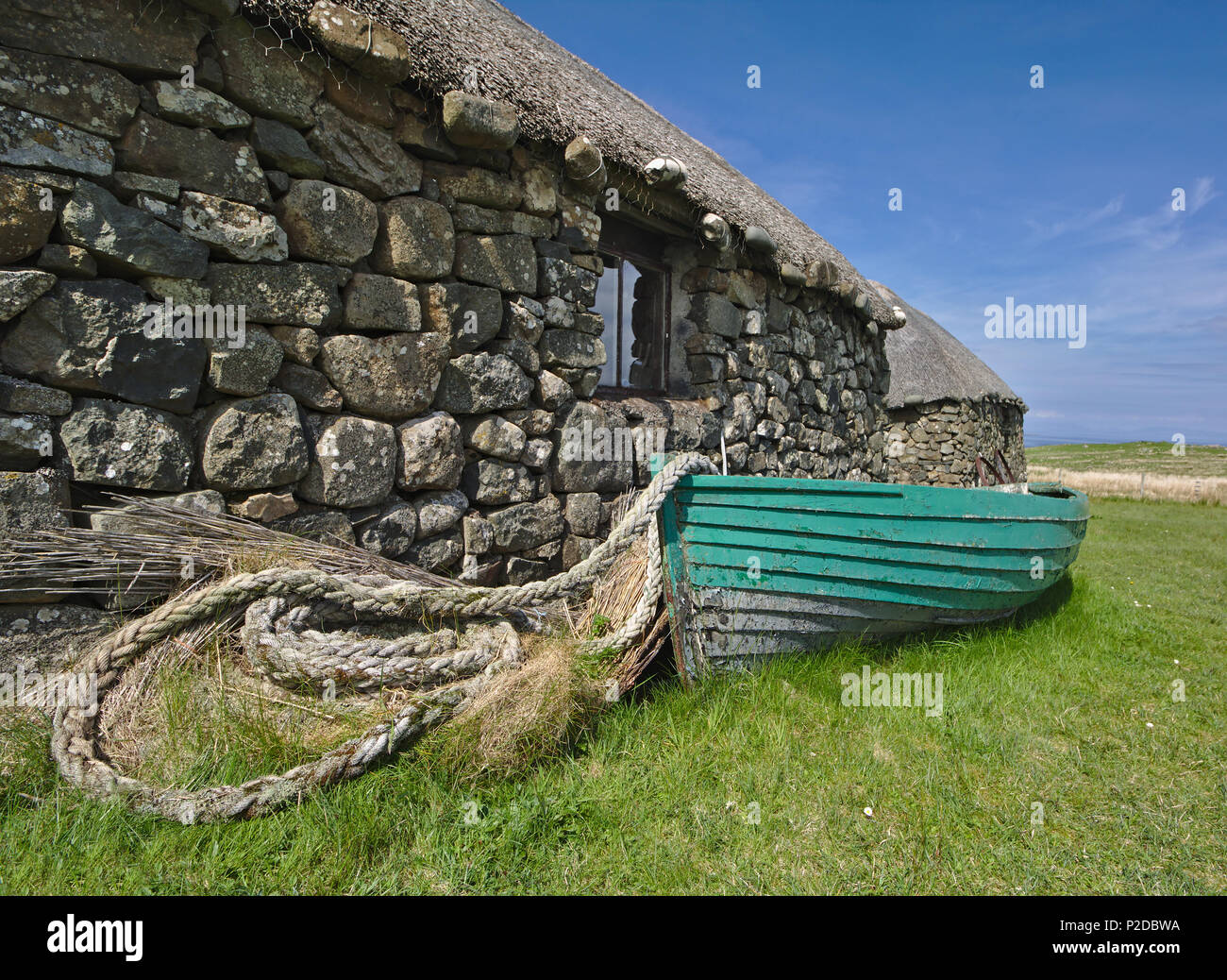Hebridean blackhouse tradicionales con techo de paja, embarcación pesquera de madera y cuerda enrollada. Foto de stock