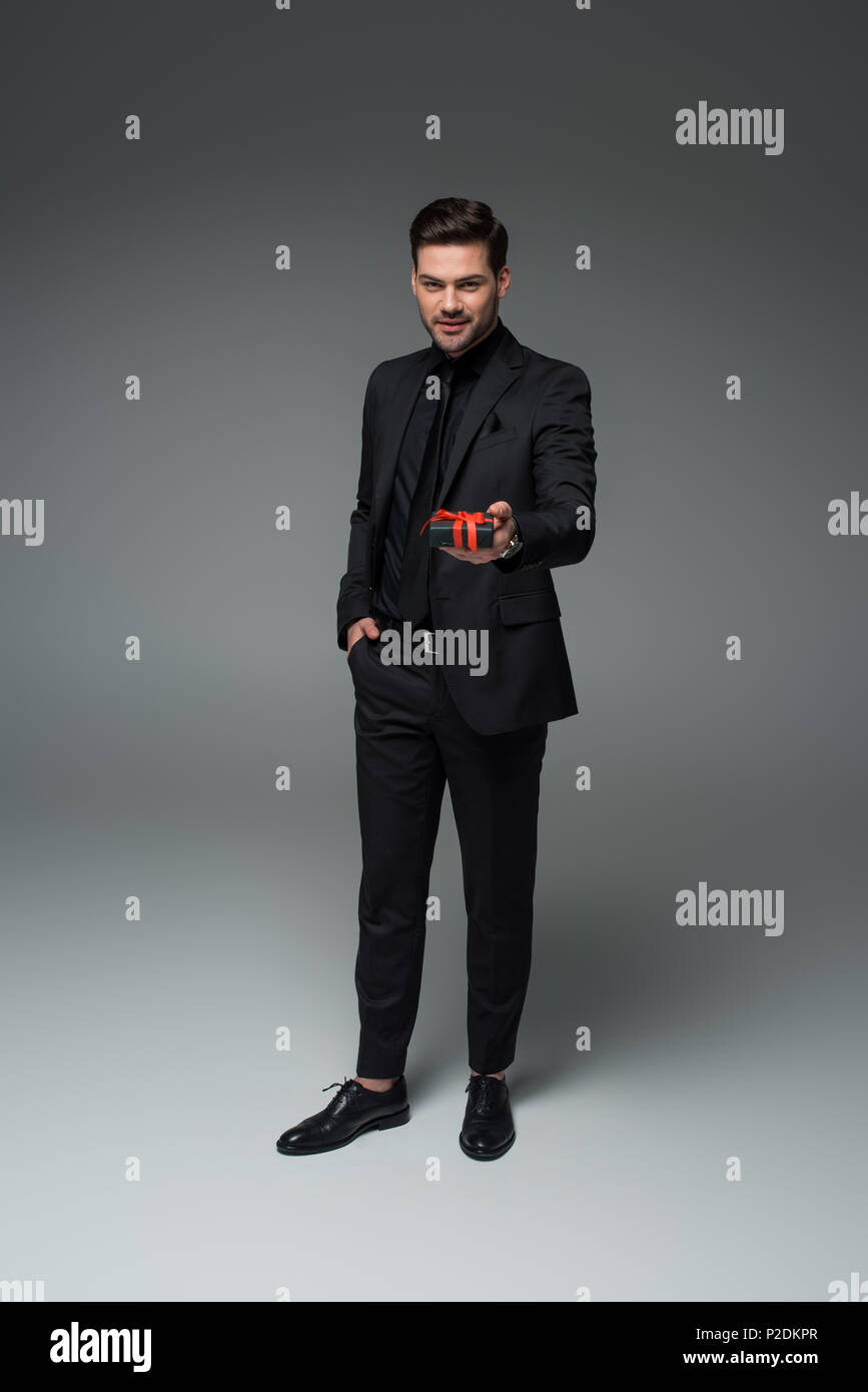 Joven hombre elegante en traje formal la celebración de caja de regalo en  color gris, día internacional de la mujer concepto Fotografía de stock -  Alamy