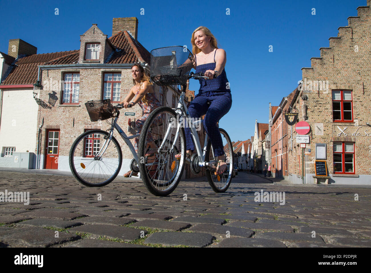 Dos jóvenes mujeres en bicicleta en una calle adoquinada, cerca de Coupure Marina, brujas, brujas, Flandes, Bélgica Foto de stock