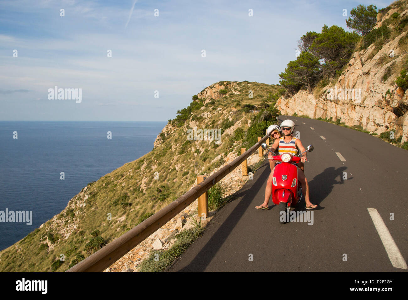 Pareja joven montando una Vespa scooter roja sobre una carretera costera a lo largo de la península de Cap de Formentor, Palma, Mallorca, Islas Baleares Foto de stock