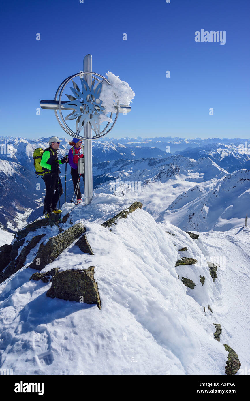 Hombre y mujer de regreso de esquí de pie en la cruz en la cima de Schneespitze, Schneespitze, valle de Stubai, Pflersch Foto de stock
