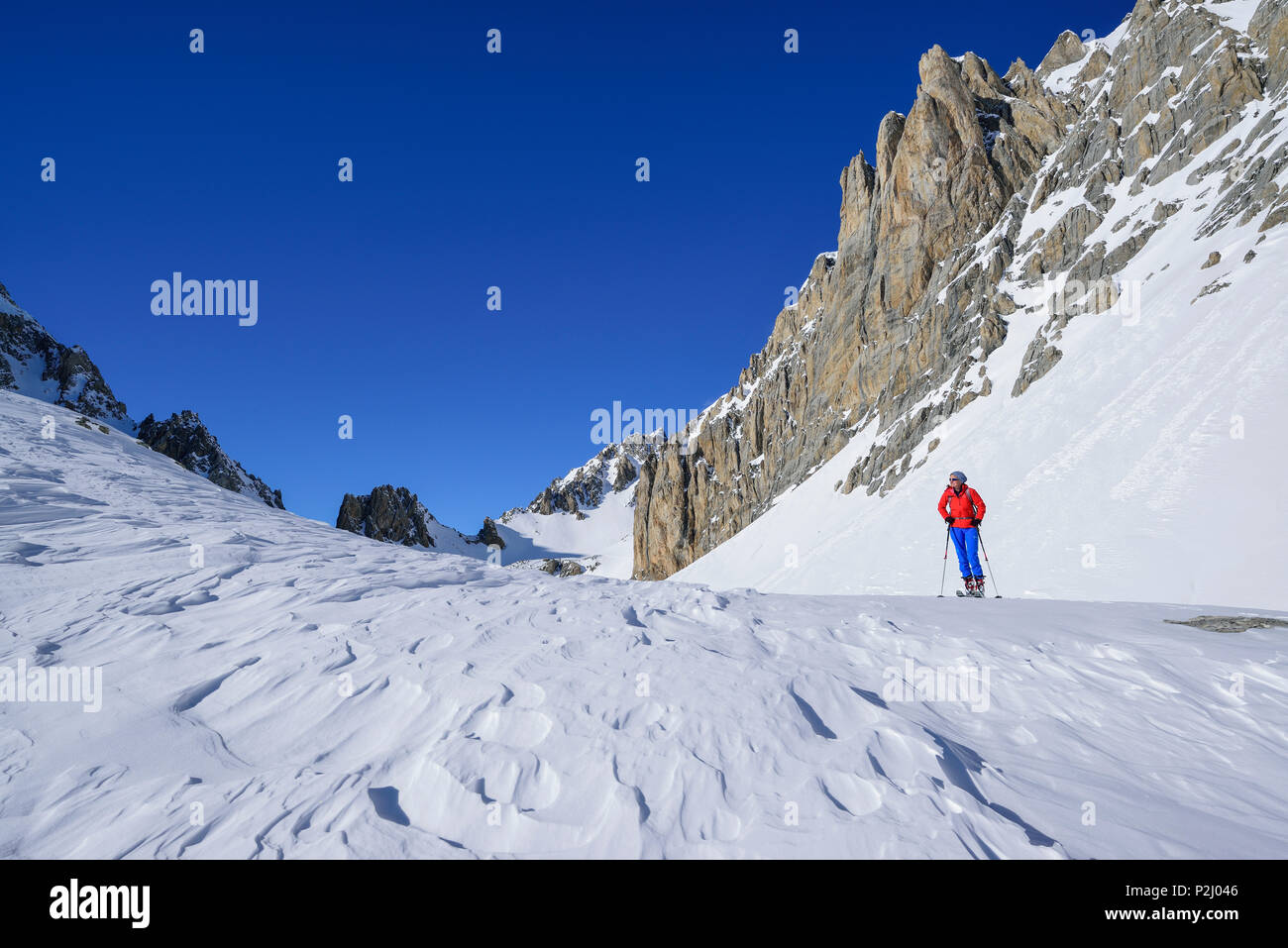 Mujer de regreso de esquí de pie debajo de pared de roca de Monte Sautron, Valle Maira, Cottian Alpes, Piamonte, Italia Foto de stock