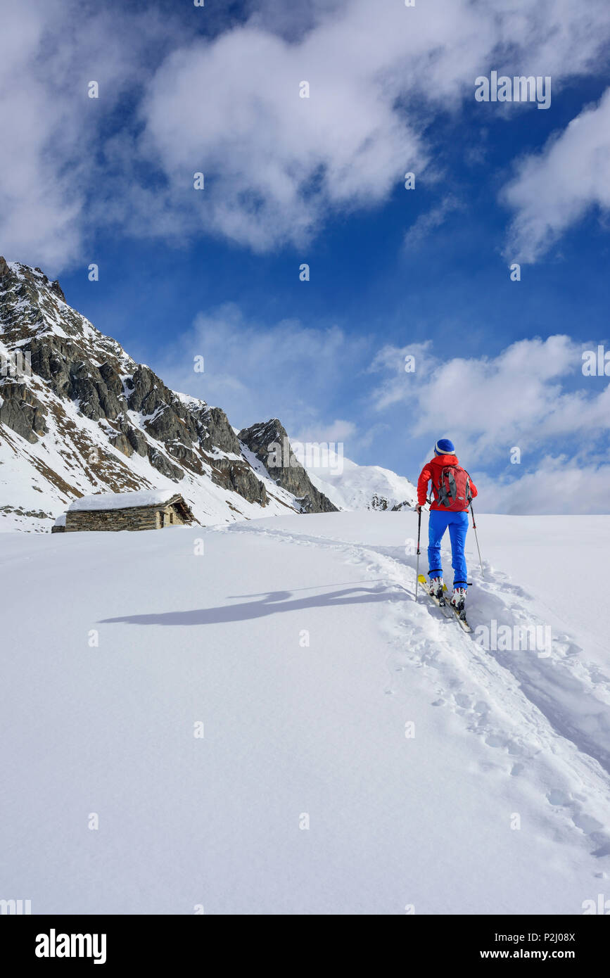 Mujer de regreso de esquí caminando hacia nevadas cabaña alpina, Monte, Valle Varaita Faraut, Cottian Alpes, Piamonte, Italia Foto de stock