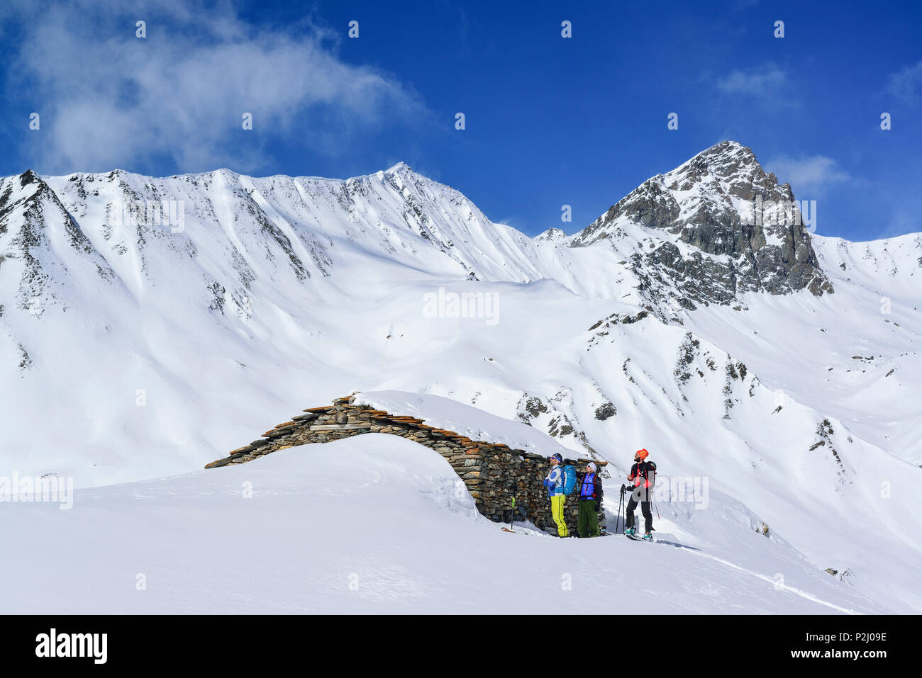 Tres personas volver de esquí de pie en frente de la cabaña alpina, Tete dell'Autaret Pelvo di Ciabriera y en segundo plano, el Monte Foto de stock