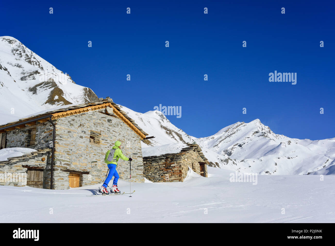 Mujer de regreso de esquí pasando cabañas alpinas y ascendiendo hacia el Monte Salza, Monte Salza, Valle Varaita, Alpes, Piedm Cottian Foto de stock