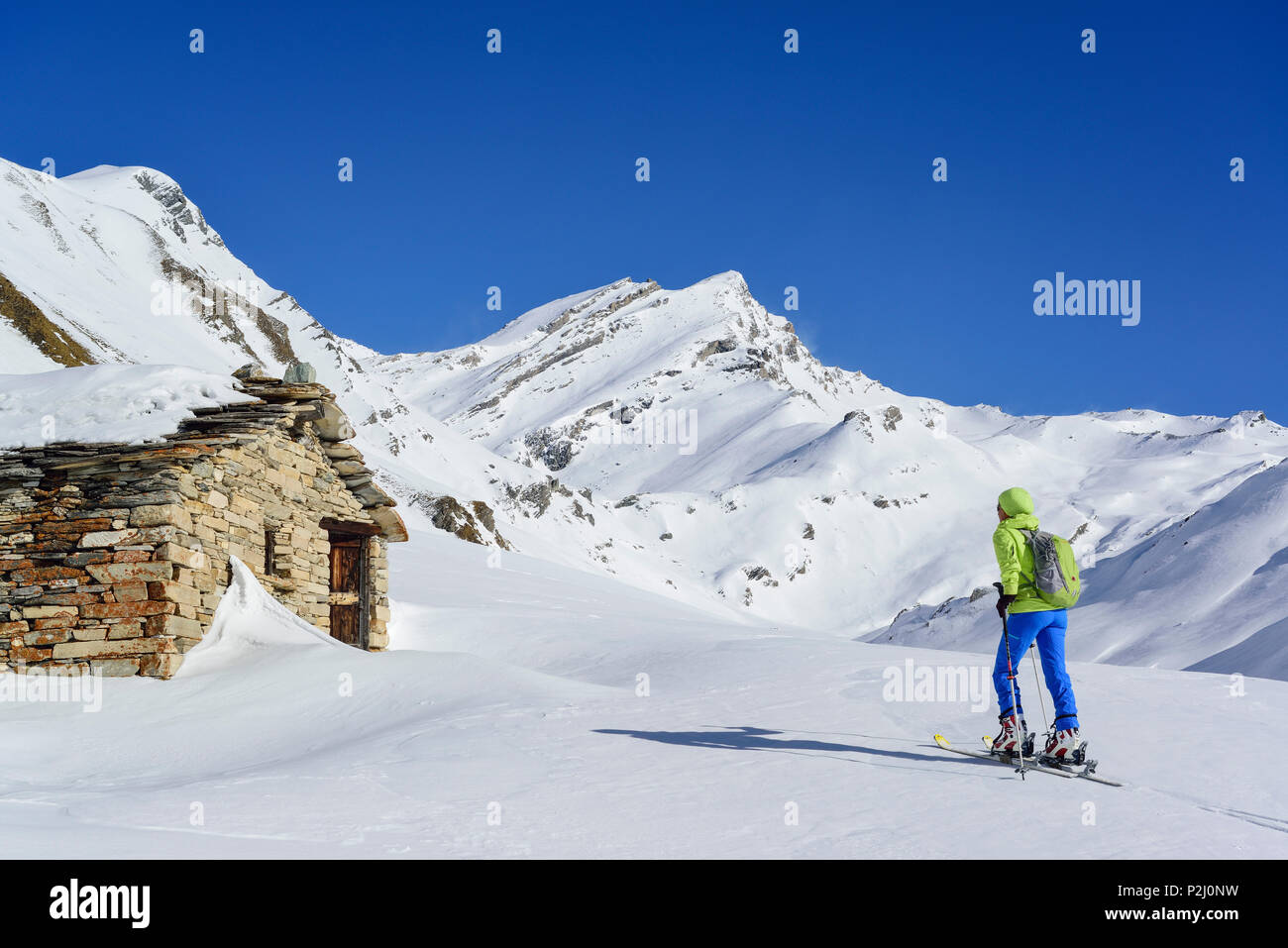 Mujer de regreso de esquí pasando cabañas alpinas y ascendiendo hacia el Monte Salza, Monte Salza, Valle Varaita, Alpes, Piedm Cottian Foto de stock